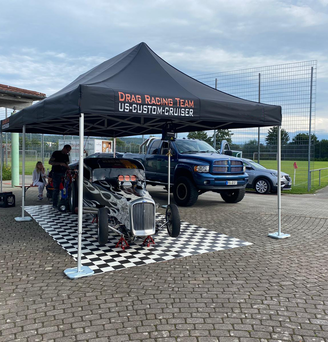 Black 8x4 gazebo with Drag Racing Team logo covers a flaming vintage car and is fixed to the ground with Ecotent gazebo weights