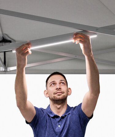 The man attaches the LED strips to the folding gazebo.